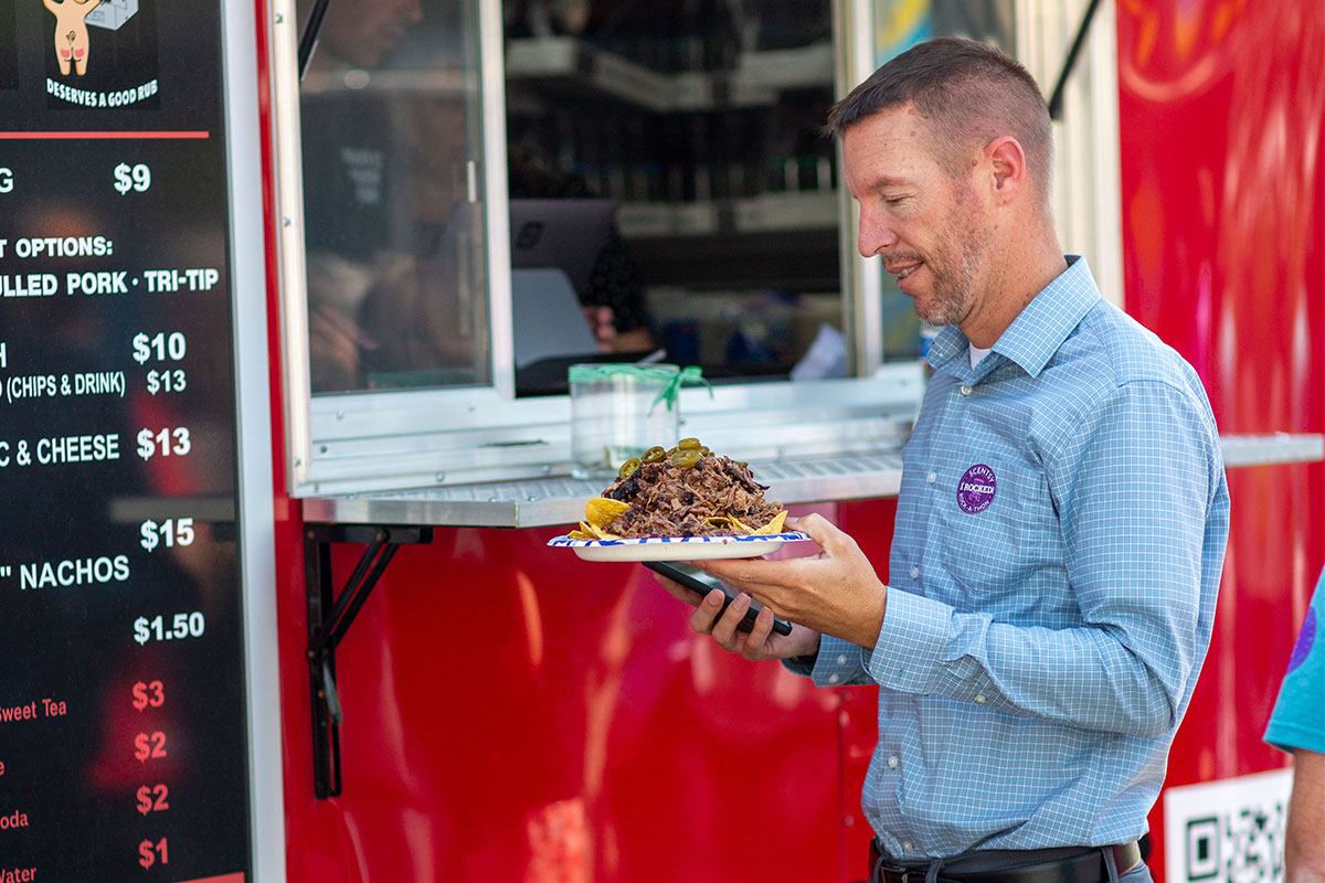 man carrying a plate of bbq brisket on a plate at food truck rally