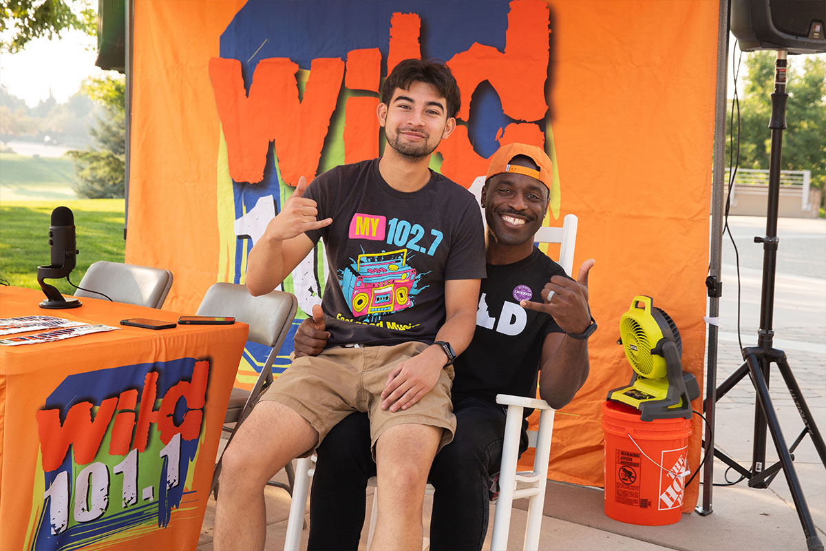 two men sitting in a rocking chair in front of radio station banner