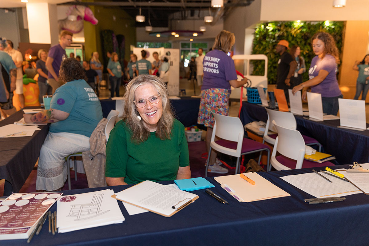 woman in green tee shirt sitting at a table with sign up forms